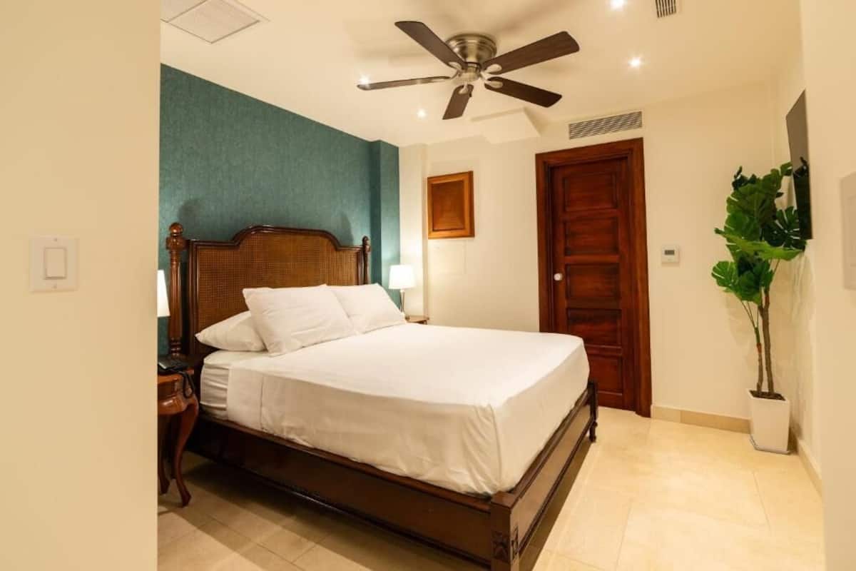 A bedroom with a wooden bed, a ceiling fan, a green accent wall, a wooden door, and a potted plant.