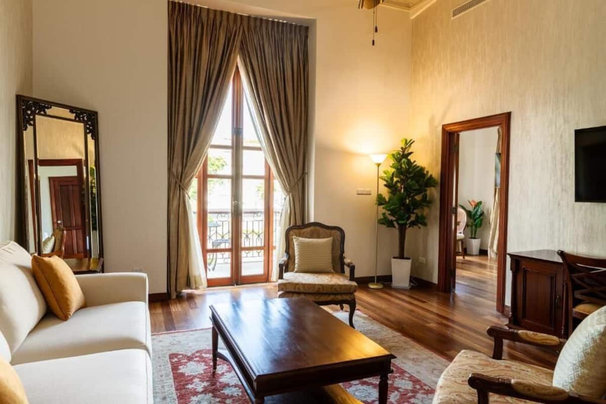 A living room with a sofa, armchair, coffee table, and a large window with curtains.