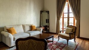Una habitación con un sofá blanco, una silla de madera, un espejo y un amplio ventanal con cortinas.