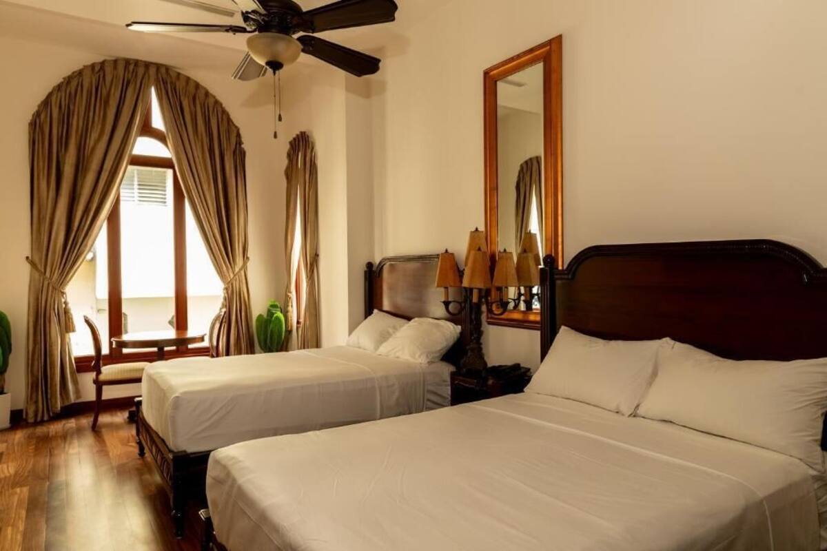 A hotel room with two beds, a ceiling fan, a large mirror, and a view of the outdoors.