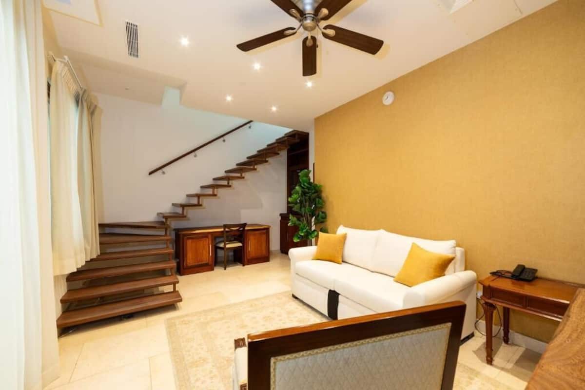 A modern living room with a staircase, a white sofa, and a ceiling fan.