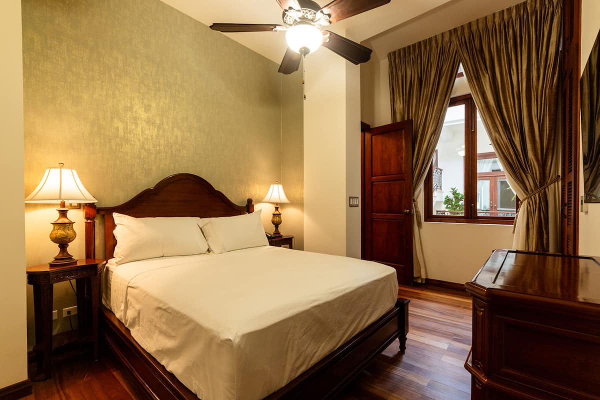 A bedroom with a wooden bed, two bedside lamps, a ceiling fan, and a window with curtains.