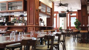 Un restaurante espacioso con altos techos de madera, numerosas mesas y sillas, y una zona de bar con estantes llenos de botellas y vasos.