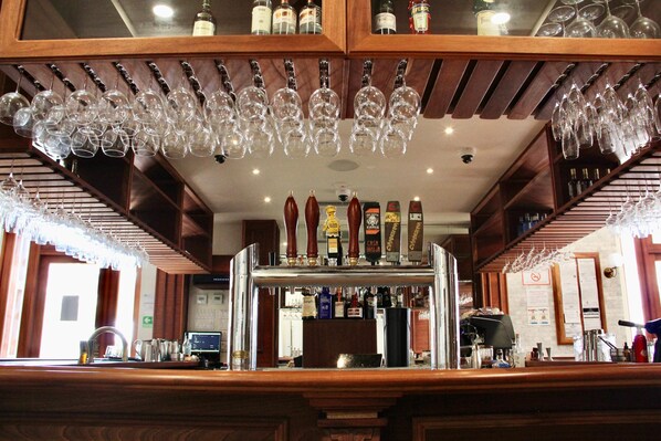 Un espace bar avec de nombreux verres à vin suspendus au plafond, une sélection de bouteilles exposées sur des étagères et un comptoir équipé de divers ustensiles de bar.