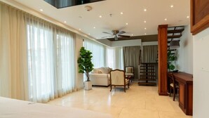 Amplia habitación de hotel con una cama grande, un área de descanso con sofá y sillones, una mesa de comedor y una escalera.