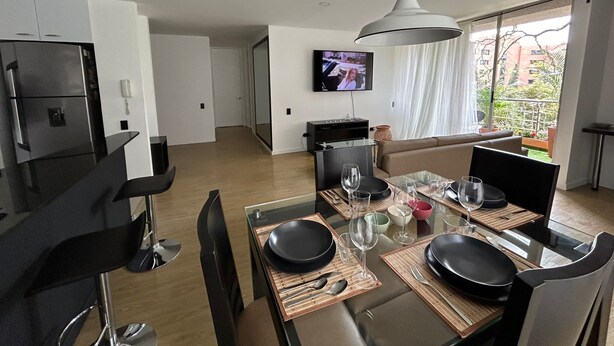 A modern living room with a dining area, a TV mounted on the wall, and a view of the outdoors. - Poblado Family and Friend Bachelor Retreat (Medellín)
