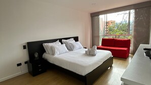 A modern hotel room with a large bed, a red sofa, and a small kitchenette. - Poblado Family and Friend Bachelor Retreat (Medellín)