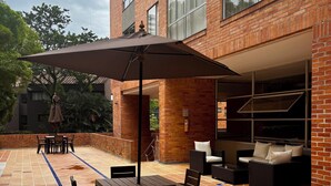 An outdoor patio with a tiled floor, a table with chairs, a large umbrella, and a seating area with sofas and a chair. - Poblado Family and Friend Bachelor Retreat (Medellín)