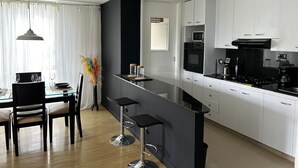 A modern kitchen with white cabinets, a black countertop, and stainless steel bar stools. - Poblado Family and Friend Bachelor Retreat (Medellín)