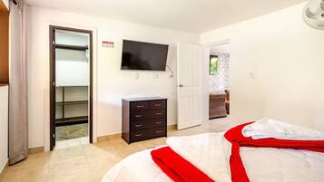 A bedroom with a bed, a TV, a wardrobe, and a door leading to a balcony.