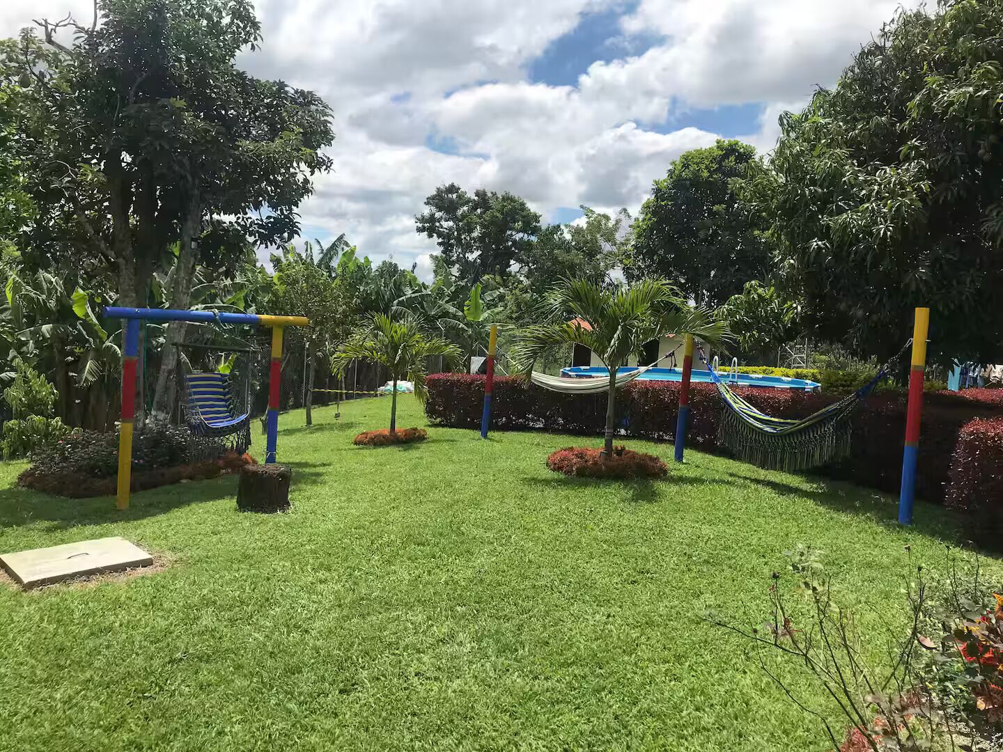 Un jardín bien cuidado con un columpio, una hamaca y una pequeña zona de piscina.