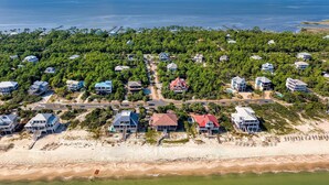 An aerial view of a coastal residential area with houses, a beach, and a pier.