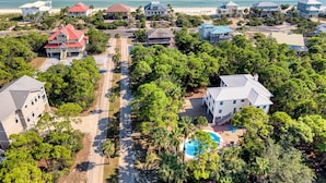 An aerial view of a coastal residential area with houses, a swimming pool, and a beach.