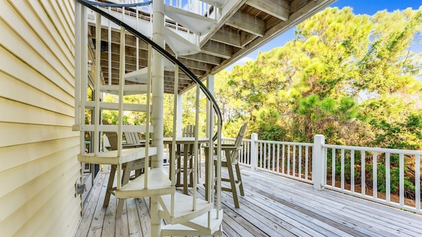 A wooden deck with a spiral staircase leading to a covered area, surrounded by trees.