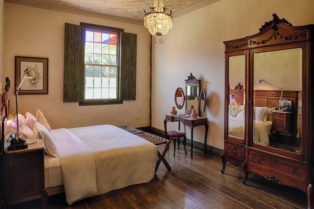 A bedroom with a bed, dresser, vanity, and a large mirror.