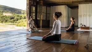 Yogatime i et rustikt rum med trægulve og store vinduer med udsigt over et smukt landskab.