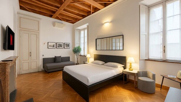 Een slaapkamer met een bed, nachtkastjes, een bank, een stoel, een televisie en een open haard.