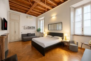 Een slaapkamer met een bed, nachtkastjes, een bank, een stoel, een televisie en een open haard.