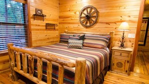 Ein Schlafzimmer in einer Holzhütte mit einem Bett, einem Nachttisch, einer Lampe und einer Wanduhr.