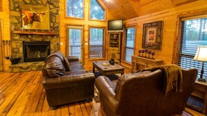 Ein gemütliches Blockhaus-Interieur mit Kamin aus Stein, Ledersofas und einem Fernseher.