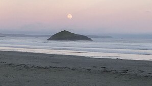 Una platja amb un petit turó i la lluna al cel.