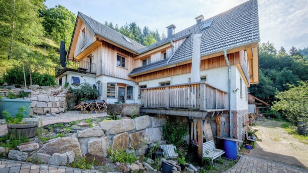 Ein Holzhaus mit Balkon, Steinunterbau und einem Garten.