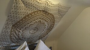 Ein ordentlich bezogenes Bett mit gestreifter Bettwäsche, ein grünes Handtuch und eine Wandteppich-Dekoration.