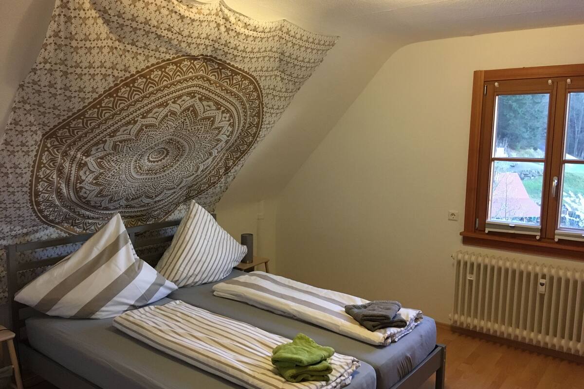 A bedroom with a bed, pillows, a blanket, a radiator, and a window with a view.