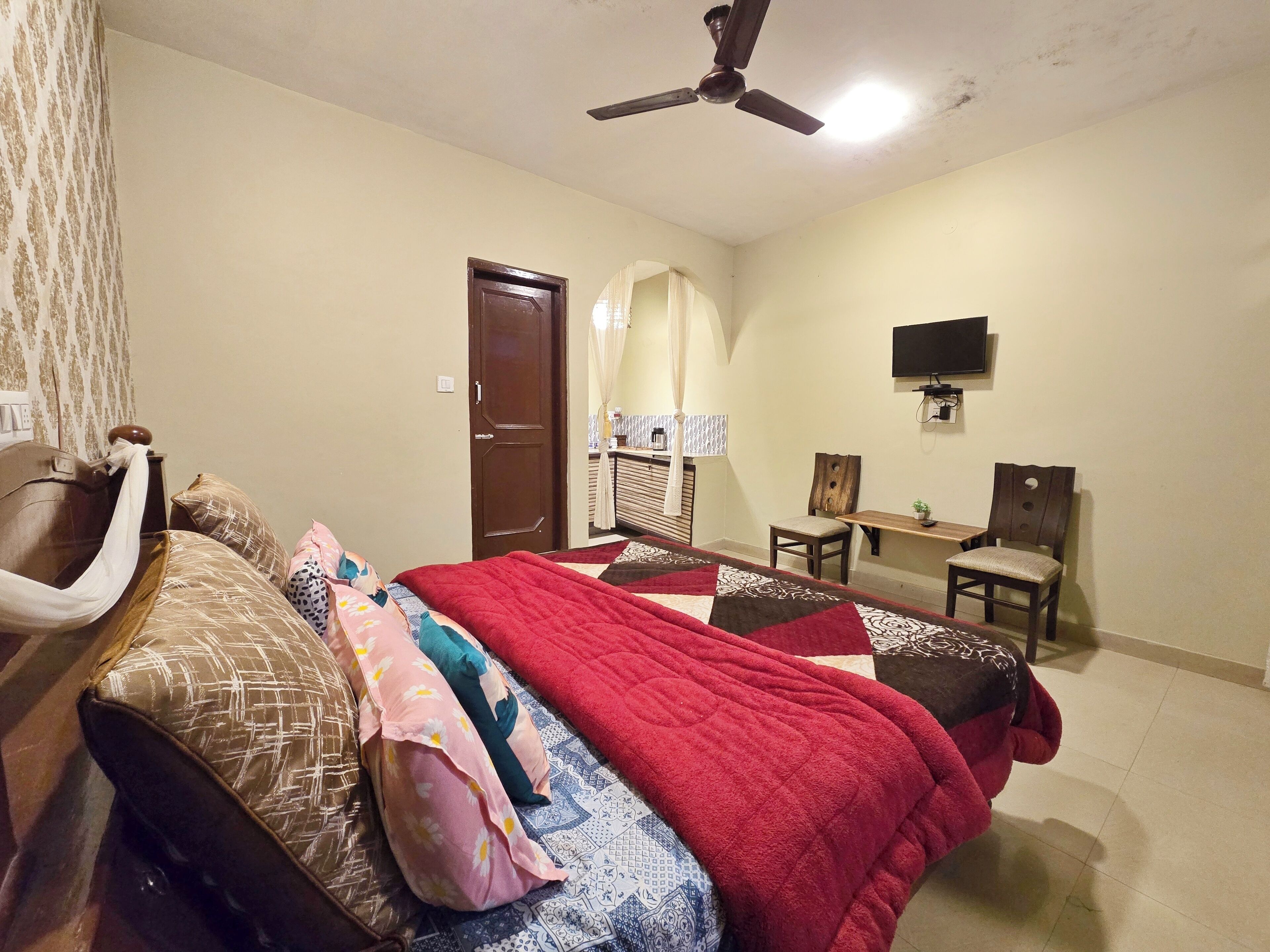 A bedroom with a bed, a desk, a chair, a television, and a ceiling fan.