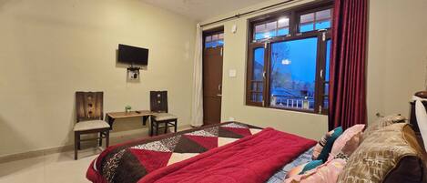 A bedroom with a bed, a desk, a chair, a television, and a window with curtains.
