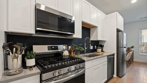 Une cuisine moderne avec des meubles blancs, une cuisinière noire, des appareils électroménagers en acier inoxydable et un dosseret carrelé.