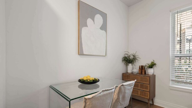 Un coin repas avec une table en verre, deux chaises, un saladier de fruits, un meuble en bois et une plante en pot.