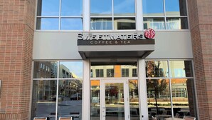 Une devanture de café Sweetwaters Coffee & Tea avec une façade en verre, des places assises à l’extérieur et une façade en briques.