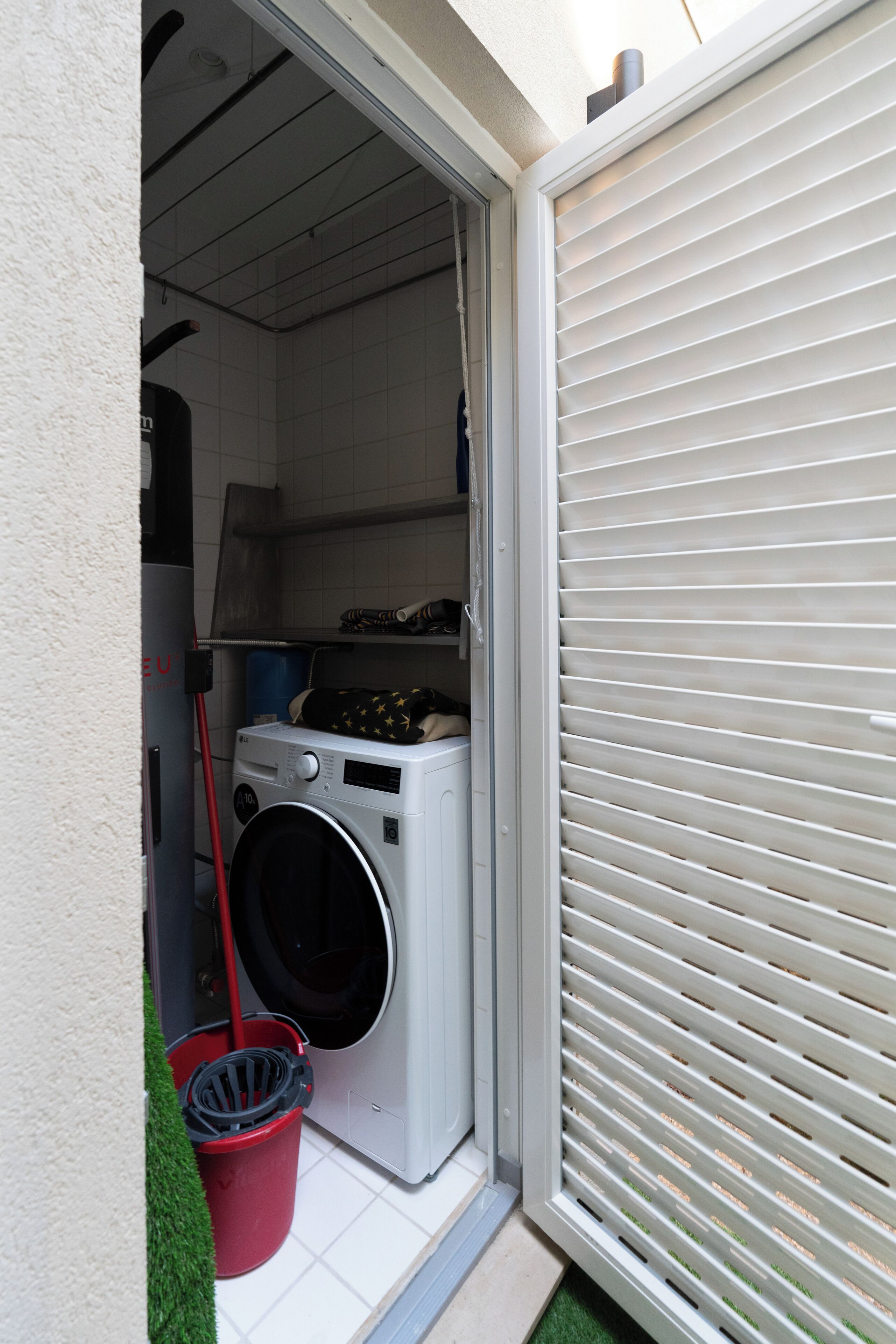 A laundry area with a washing machine, a red bucket, and a broom.