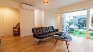 Ein modernes Wohnzimmer mit einer Ledersofa, einem Holztisch und einer Glastür, die auf einen Balkon mit Gartenmöbeln führt.