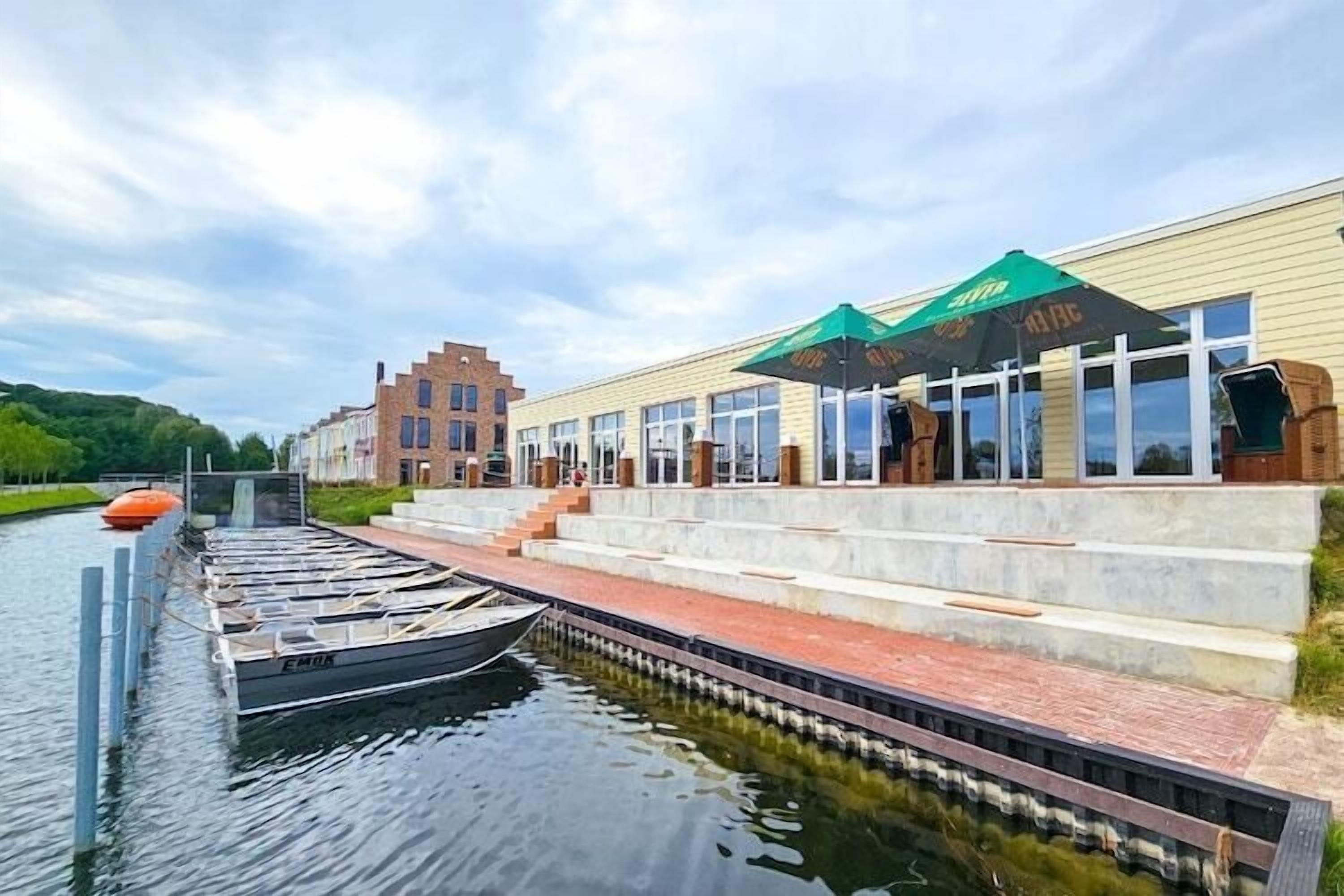 Un edifici al costat del riu amb un moll, escales cap a una zona coberta, i un pont al fons.
