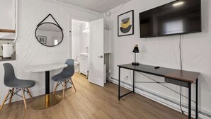 Ein modernes Zimmer mit einem runden Tisch, zwei Stühlen, einem Schreibtisch, einem Flachbildfernseher und einem gerahmten Kunstwerk an der Wand.