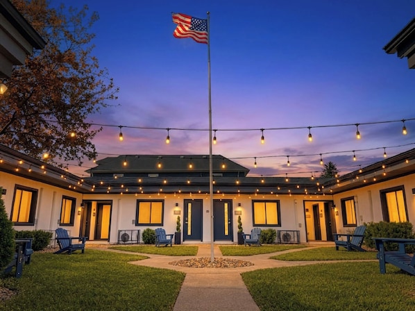 A hotel with a flagpole, string lights, and outdoor seating. - Franklin Park Studio Kitchen + Workspace (Columbus)