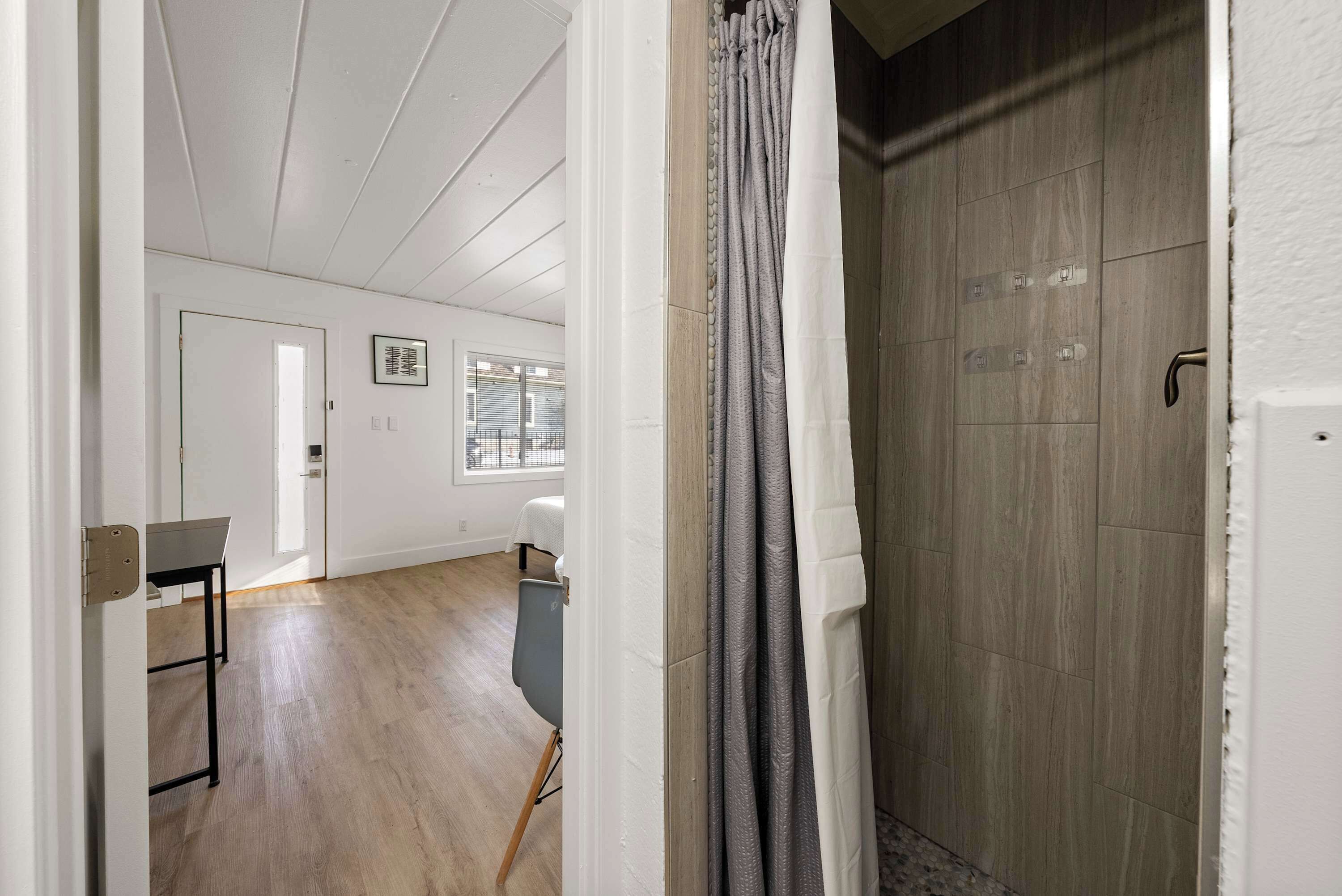 A modern interior with a wooden floor, a dining area with a table and chairs, and a shower area with a curtain.