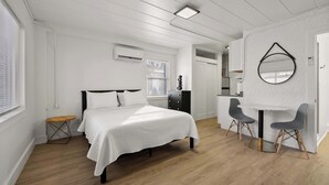Ein Schlafzimmer mit einem Bett, einem kleinen Holzschemel, einem Schreibtisch mit zwei Stühlen und einem Spiegel an der Wand.