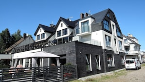 A modern two-story house with a balcony, a covered outdoor seating area, and a parked van.
