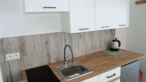 A kitchen with white cabinets, a stainless steel sink, and a kettle on the counter.
