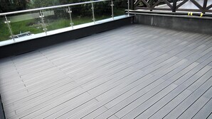 Een houten terras met glazen hekwerk met uitzicht op een gazon.