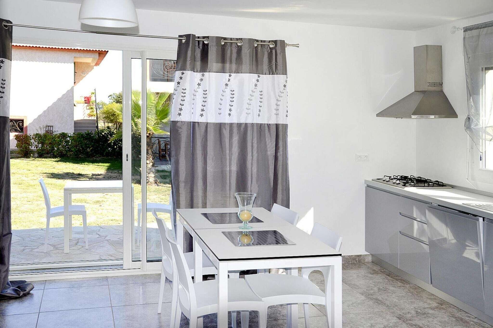 Une cuisine moderne équipée d’une cuisinière à gaz, d’une hotte en acier inoxydable et d’une porte en verre donnant sur un espace extérieur aménagé pour se détendre.