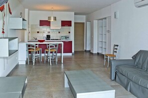 Cozinha moderna com armários vermelhos e brancos, micro-ondas e fogão a gás. Há uma sala de jantar com mesa e cadeiras, e um sofá cinza na sala de estar.