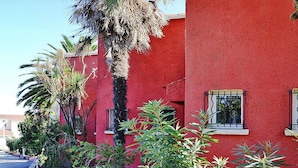 A red building with windows, surrounded by various plants. - Rés. Marea Resort, Santa-Lucia-di-Moriani (Santa-Lucia-di-Moriani)