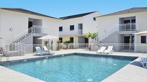 A swimming pool with white railings, lounge chairs, and a two-story building with balconies. - Rés. Marea Resort, Santa-Lucia-di-Moriani (Santa-Lucia-di-Moriani)