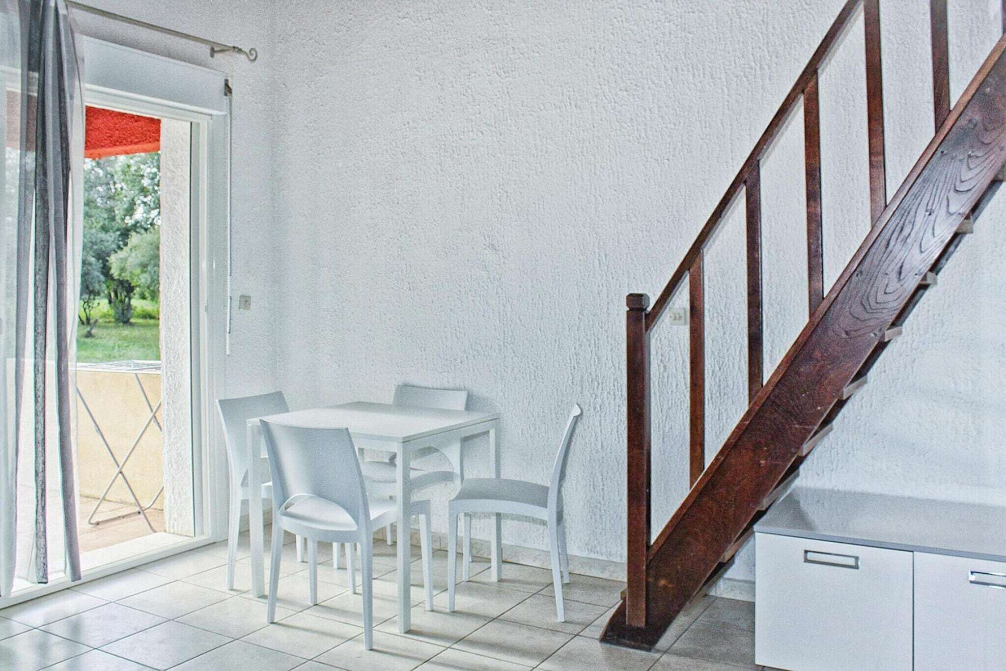 Une pièce comprenant une table à manger et des chaises, un escalier en bois et une porte-fenêtre coulissante donnant sur un espace extérieur.
