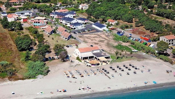 An aerial view of a coastal area with a beach, several buildings, and parked vehicles. - Rés. Marea Resort, Santa-Lucia-di-Moriani (Santa-Lucia-di-Moriani)