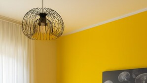 Une chambre d’hôtel avec un mur jaune, un lit avec une tête de lit marron et une table de chevet avec une lampe.
